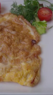 Çok güzel pişirilmiş, mükemmel altın bir omlet, canlı turuncu bir tabakta servis edilir.