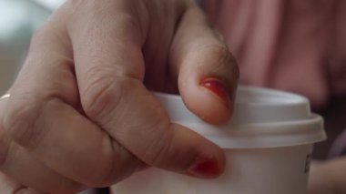 Beyaz bir kahve fincanını sıkıca kavrayan bir el rahatlamış ve sıradan bir kahve anı sergiliyor.