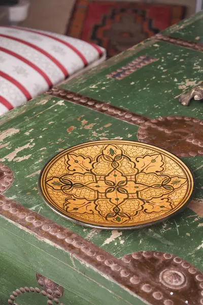 Şaşırtıcı bir şekilde işlenmiş pirinç levha antika yeşil bir sandığın üzerinde zarif bir şekilde duruyor.