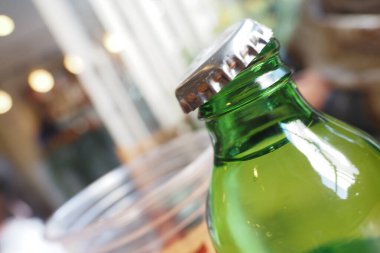 Bu, samimi bir kafe atmosferinde geçen yeşil bir şişenin kapağını gösteren yakın plan bir görüntü.