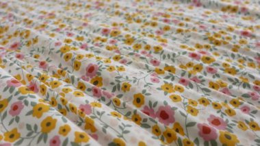 Yatak odasında çiçekli yorgan ve yastıklı bir yatak var. Odada ahşap eşyalar ve ahşap döşemeler var, rahat bir atmosfer yaratıyor.