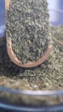 Ahşap bir kaşıkta güzelce sergilenen çeşitli kurutulmuş yeşil otların detaylı yakın plan görüntüsü.
