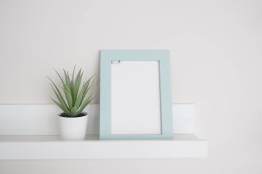 Bu temiz ve modern bir raf güzel bir saksı bitkisinin yanında boş bir çerçeve sergiliyor.