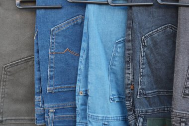 Perakende mağazasındaki askılarda çeşitli renklerde kot pantolonlar sergileniyor.