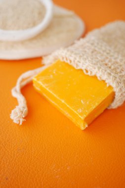 Parlak turuncu bir sabun doğal bir lif torbasına yerleştirilir ve güzel bir sunum yaratır.