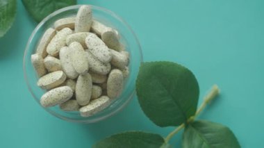 Cam bir kasede sergilenen bitkisel tabletler, güzel bir sunum için yeşil yapraklarla tamamlanmış.