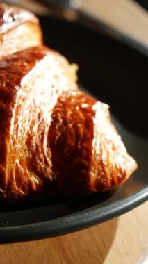 Altın bir kruvasan siyah bir tabakta duruyor. Yumuşak bir şekilde aydınlanıyor.