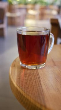Ahşap bir masaya konmuş cam bir fincanda servis edilen taze demlenmiş çay fincanı.