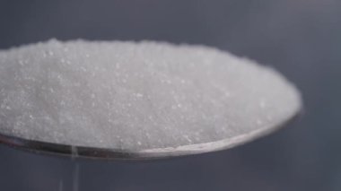 Bu, metal kaşığın üzerinde duran beyaz granüllü şekerin detaylı ve yakından çekilmiş görüntüsü.
