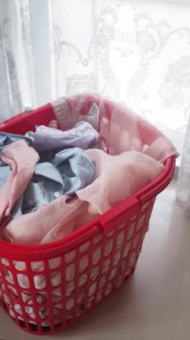 Taze, renkli tekstil dolu parlak kırmızı bir çamaşır sepeti bir pencerenin yanında duruyor.