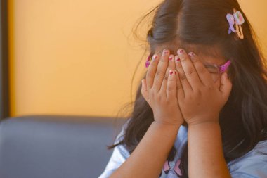 a upset child girl cover her face with hand .
