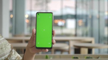 Bir el, modaya uygun bir atmosferde canlı yeşil bir ekran içeren akıllı bir telefonu tutuyor.