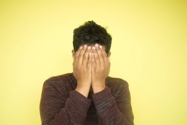 Bir birey neşeli bir şekilde yüzünü parlak sarı bir arka plana karşı açık yüreklilikle kapatıyor.