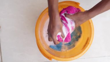 İki el güçlü bir şekilde sabunlu suyla dolu bir kovada çeşitli eşyalar ovalıyor.