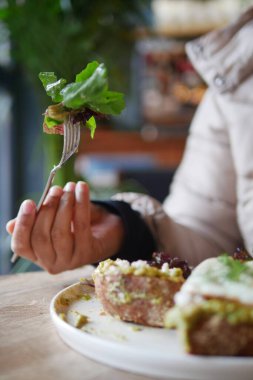 Bir el zarif bir şekilde taze yeşillikleri olan parlak bir çatalı tutar, keyifli bir yemeğin tadını çıkarmaya hazırdır.