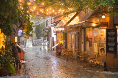 Büyüleyici sokak sahnesi yağmurda çekildi, ışıklar ve açık hava oturma yerleriyle süslendi..