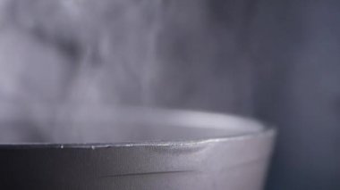 Yakın plan, tencereden çıkan buharı koyu bir arka plana doğru yansıtıyor ve etkiyi arttırıyor.