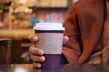 Bir el sıcak bir kafe atmosferinin davetkar sıcaklığında bir kahve bardağını nazikçe tutar.