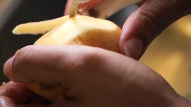 Bir çift el mutfak soyacağı kullanarak patatesi ustalıkla soyuyor ve pişirmeye hazırlıyor.