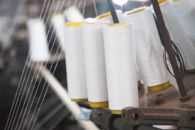 Görüntü, endüstriyel tekstil makinesindeki beyaz iplik makaralarının yakın çekimini gösteriyor.