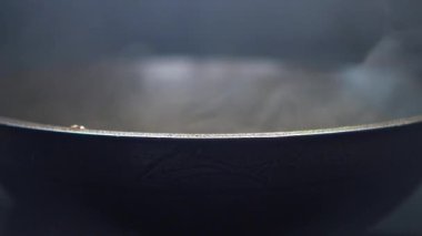 Buharı yükselen siyah bir tavanın yakın çekimi yemek pişirme etkinliğini gösteriyor..