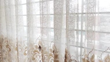 Pencerenin önünde bej ve beyaz perdeler.