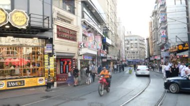 Canlı şehir caddesi çeşitli dükkanlar ve araçlarla dolup taşıyor.