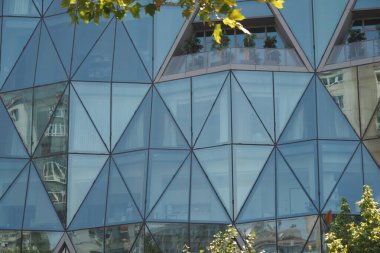 Mavi karolar çarpıcı modern mimari ortamda tüylü beyaz bulutları yansıtıyor.