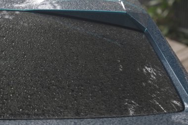 Su damlacıkları yağmurdan sonra arabanın ön camında toplanarak çevreyi bulanık bir şekilde görüyorlar. Islak yüzey huzurlu bir atmosfer yaratır..