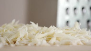 Bir insan, sıcak ve davetkar bir mutfakta peyniri ustalıkla öğütür. Peynirin dokusu ve tazeliği vurgulanıyor ve bu bileşenin lezzetli yemekler için önemini gösteriyor..
