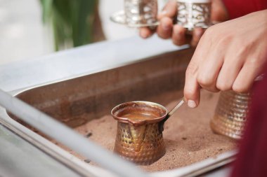 Bir el kumdaki metal bir tencerede kahve karıştırıyor..