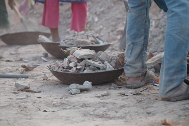 İşçiler inşaat alanında metal kaseler kullanarak moloz taşıyorlar..