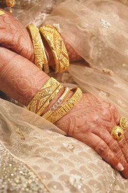 Karmaşık kına tasarımları ve çoklu altın bilezikler gösteren eller..