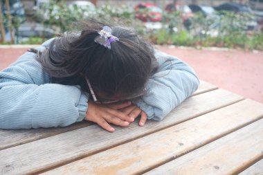 Genç bir kız ahşap bir masaya eğiliyor, kafası eğik, dalgın dalgın dalgın bakıyor..