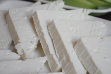 Taze kesilmiş peynir parçaları, sebzeli bir tabakta..