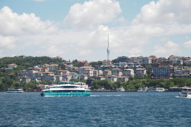 Istanbuls 'un yeşil kıyı şeridinde açık gökyüzünün altında bir feribot süzülüyor.