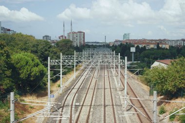 Şehir binaları ve ağaçlarla çerçevelenmiş çelik raylar mesafeye kadar uzanıyor..