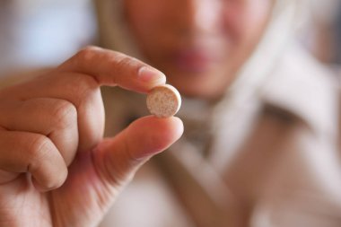 Bir kadın parmağıyla küçük yuvarlak bir tablet sergiliyor..