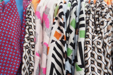 Farklı renklerde örülmüş kazaklar açık hava pazarında parlak bir şekilde asılı duruyor..