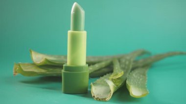 Bu ekranda taze aloe vera yapraklarının yanında yeşil bir dudak kremi var..