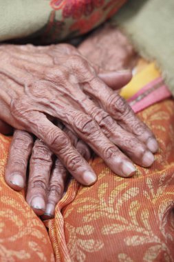 Karmaşık kırışıklıkları olan yaşlı eller renkli kumaş üzerinde dinleniyor..