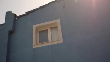 Mavi bir bina duvarı tek bir pencere ve güneş ışığı yansımalarını gösterir..