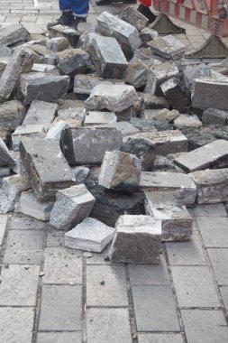 İşçiler yere saçılmış kaldırım taşları olan bir sokağı onarıyor..