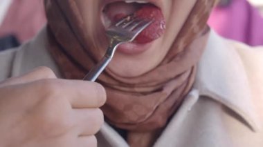 Bir insan hareketli bir pazar atmosferinin keyfini çıkarırken canlı bir meyvenin tadına bakar..