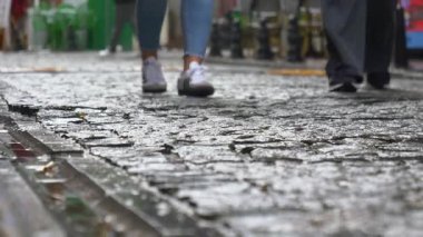 Yayalar yağmurdan sonra parlayan kaldırım taşları yolunda yürürler..