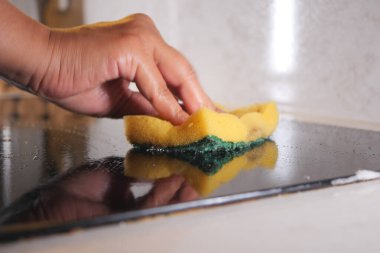 Bir insan ocağın üstünü sarı bir süngerle dikkatlice ovalıyor..