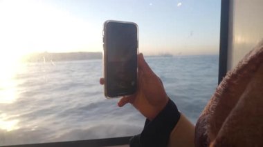 Suyun üzerinde gün batımını kaydetmek için bir telefon tutuyorum..