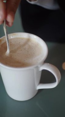 Bir el sıcak bir masada köpüklü bir fincan kahve karıştırır..