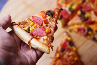 Bir el, sebze ve pepperoniyle kaplı bir dilim pizzayı tutar..