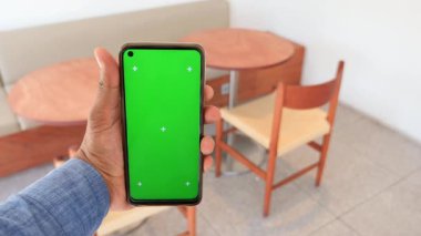 Bir kafede canlı yeşil ekranlı akıllı telefonunu sergileyen bir kişi....